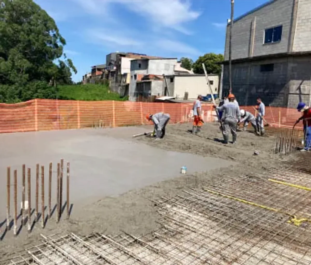 Equipe sarrafeando concreto fresco em laje com tela de aço